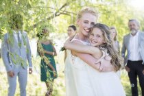 Novia abrazando dama de honor en la recepción de la boda en el jardín doméstico - foto de stock