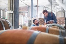 Male winemakers with digital tablet checking wood casks — Stock Photo