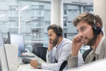Uomini d'affari con dispositivi a mani libere che parlano al telefono mentre lavorano al computer in ufficio — Foto stock