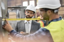 Manager watching steel worker with tape measure in factory — Stock Photo