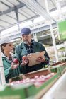 Manager mit Klemmbrett und Arbeiter begutachten rote Äpfel in Lebensmittelfabrik — Stockfoto