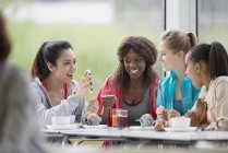 Mulheres sorridentes bebendo café e suco usando telefone celular no café pós treino — Fotografia de Stock
