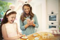 Mother and daughter wearing costume rabbit ears coloring Easter eggs and cookies — Stock Photo