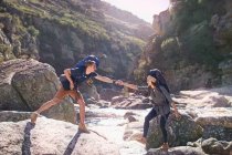 Giovane uomo aiutare fidanzata escursioni, attraversando rocce soleggiate nel torrente — Foto stock