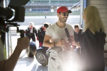 Репортёр женских новостей берёт интервью у гонщика Формулы 1 в ремонтном гараже — стоковое фото