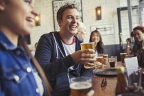 Sonriente hombre bebiendo cerveza con amigos en la mesa en el bar - foto de stock