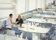 Empresario y empresaria discuten papeleo en mesa en espacio de trabajo compartido - foto de stock