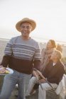 Portrait smiling senior man barbecuing with friends on sunset beach — Stock Photo