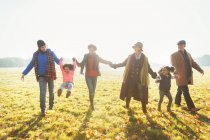 Famille multi-génération ludique marchant dans l'herbe ensoleillée du parc d'automne — Photo de stock