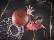 Vista aérea joven jugador de baloncesto masculino saltando para rebotar la pelota en el borde del baloncesto - foto de stock