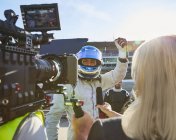 Periodista de noticias y camarógrafo entrevistando a un conductor de fórmula vitoreando, celebrando la victoria - foto de stock