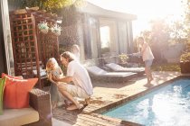 Playful daughter with squirt gun spraying father and sister with water at sunny poolside — Stock Photo