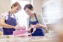 Female caterers finishing pink wedding cake in kitchen — Stock Photo