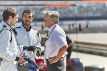 Gerente e Fórmula 1 pilotos de carros de corrida falando sobre pista esportiva — Fotografia de Stock