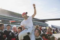 Equipe de corrida de Fórmula 1 carregando motorista torcendo nos ombros, celebrando a vitória na pista de esportes — Fotografia de Stock