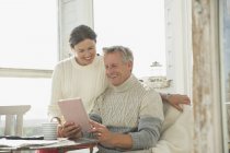 Smiling mature couple using digital tablet at table on sunny sun porch — Stock Photo