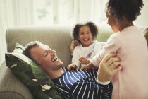 Gioco multi-etnico padre e figlie solletico e ridere sul divano — Foto stock