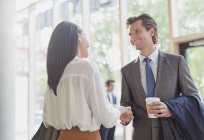 Businessman with coffee and businesswoman handshaking in office lobby — Stock Photo