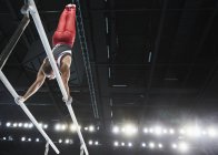 Male gymnast performing upside-down handstand on parallel bars in arena — Stock Photo