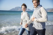 Young couple holding hands and walking on beach — Stock Photo