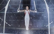 Male gymnast balancing with arms outstretched on gymnastics rings in arena — Stock Photo
