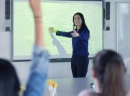 Smiling female science teacher leading lesson at projection screen in classroom — Stock Photo