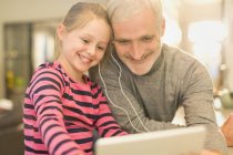 Souriant père et fille partageant écouteurs, regarder la vidéo sur tablette numérique — Photo de stock