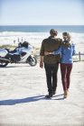 Casal sênior afetuoso andando na praia ensolarada em direção a motocicleta — Fotografia de Stock