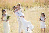 Подружка невесты и подружка невесты смотрят и смеются, молодая пара обнимается на лугу — стоковое фото