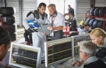 Manager e pilota di formula uno che discutono di diagnostica telemetrica in officina di riparazione — Foto stock
