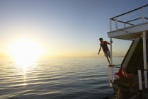 Homem inclinado no barco de verão trilhos sobre o pôr do sol oceano — Fotografia de Stock