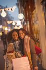Retrato sorrindo jovens amigas com sacos de compras na rua noturna urbana — Fotografia de Stock