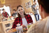 Mujer sonriendo a un amigo, comiendo en la mesa de la cabaña - foto de stock