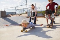 Amigos juguetones en patinetas en el soleado parque de skate - foto de stock