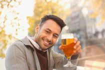 Portrait smiling young man drinking beer at autumn sidewalk cafe — Stock Photo
