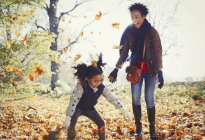 Mãe e filha brincalhão jogando folhas de outono no parque ensolarado — Fotografia de Stock