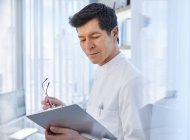 View of man in laboratory holding glasses and chart, looking away — Stock Photo