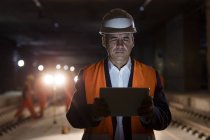 Capataz masculino grave usando tablet digital no local de construção escuro — Fotografia de Stock