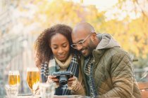 Молоді пара перегляду цифрової камери і пити пиво в осінній тротуарі кафе — стокове фото