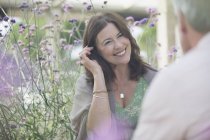 Усміхнена зріла жінка розмовляє з чоловіком на дворику з фіолетовими квітами — стокове фото