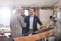 Male carpenters handshaking with satisfied customer next to wood kayak in workshop — Stock Photo