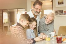 Male gay parents and children using cell phone at kitchen counter — Stock Photo