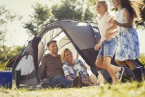 Parents watching happy daughters running around sunny campsite tent — Stock Photo