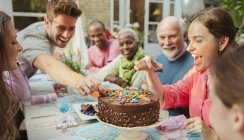 Family reaching for candy on chocolate birthday cake at patio table — Stock Photo