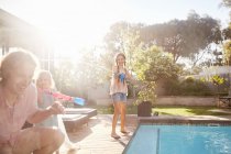 Hija con pistola de agua chorreando padre con agua en la soleada piscina de verano - foto de stock