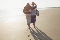 Pareja madura abrazándose y caminando en la playa soleada - foto de stock