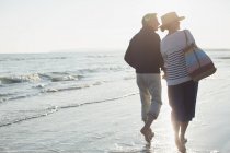 Descalzos pareja adulta caminando en la playa puesta del sol - foto de stock
