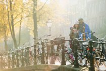 Retrato sonriente pareja joven bebiendo café a lo largo de las bicicletas en el soleado puente urbano de otoño, Amsterdam - foto de stock