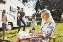 Femme souriante lisant le magazine et buvant le café dehors le camping-car ensoleillé — Photo de stock