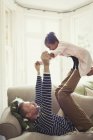 Multi-ethnic father playing, balancing daughter on legs overhead on sofa — Stock Photo